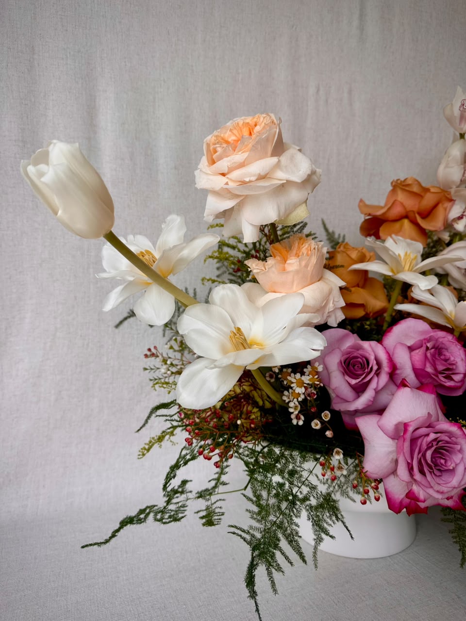 Pink-and-white parrot tulips arching from a white footed vase