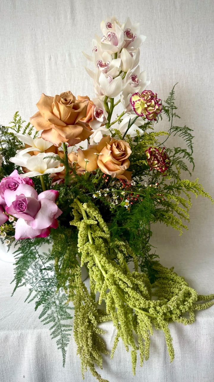 Behind the scenes: a florist's flat-lay of coral scissors, white satin ribbon, green amaranthus and peach roses on linen